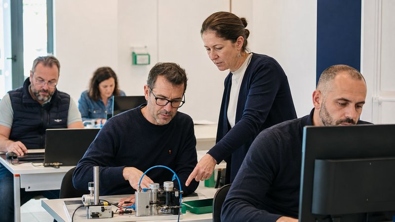 Formatrice accompagnant des stagiaires adultes sur un banc d'essai technique, en salle de formation